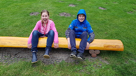 zwei Kinder sitzen auf einem Baumstamm